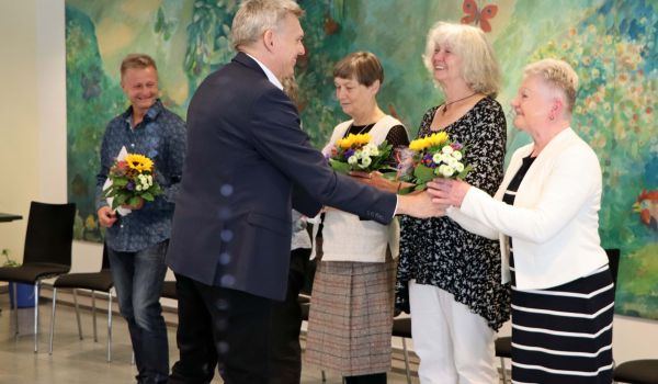 Fünf Personen stehen in einer Reihe nebeneinander. Der Bürgermeister Dr. Heiko Voigt überreicht ihnen Urkunde und Blumen.