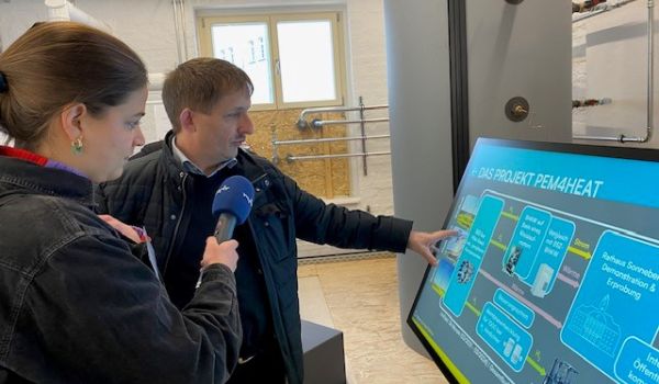 Eine Frau interviewt einen Mann, der auf einen Bildschirm zeigt.