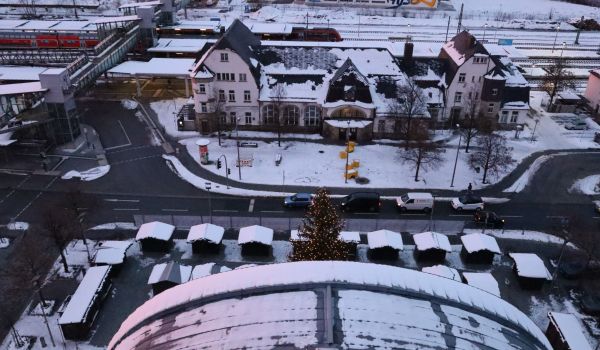 Drohnenaufnahme mit Blick auf den Bahnhof und das Rathaus. Vor dem Rathaus ist Weihnachtsmarkt. Es liegt Schnee.