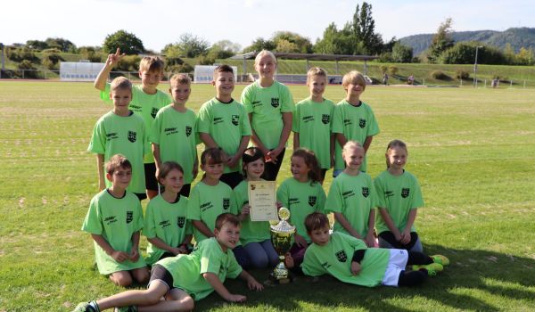 Kinder mit grünen Trikots halten stolz eine Urkunde und einen Pokal Richtung Kamera.