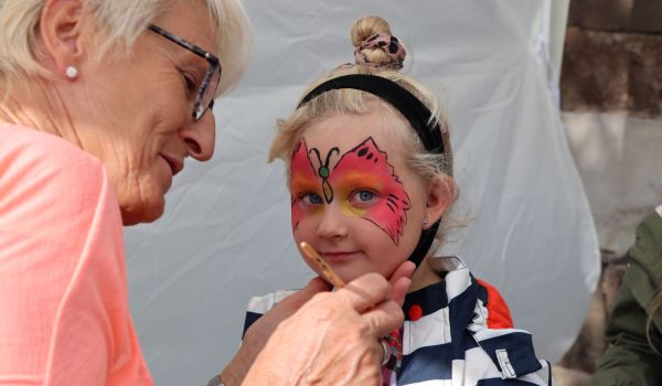 Eine Frau malt einem Kind einen roten Schmetterling ins Gesicht.