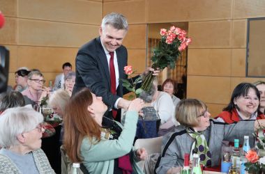 Frauen sitzen an gedeckten Kaffeetischen. Der Bürgermeister Dr. Heiko Voigt verteilt Rosen.