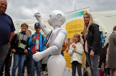 Kinder und Erwachsene stehen um einen Roboter herum.