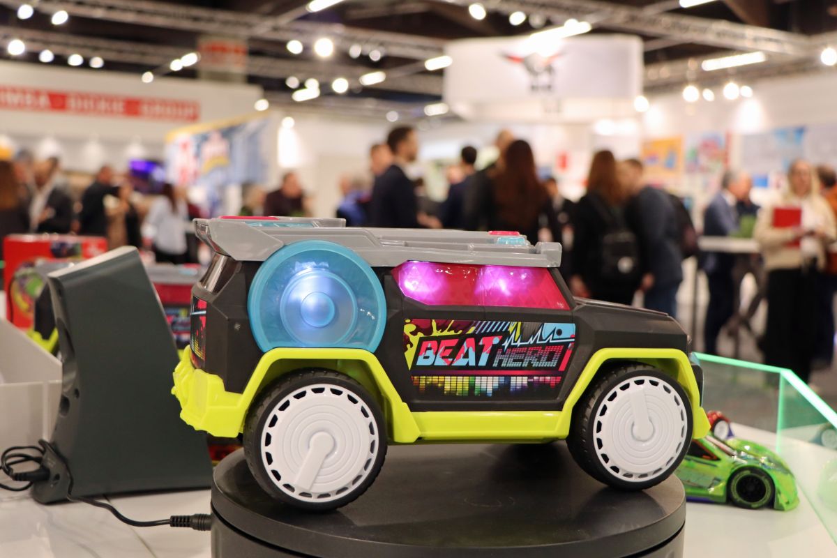 Ein Spielzeugauto mit bunten Lichtern. Im unscharfen Hintergrund stehen viele Menschen.