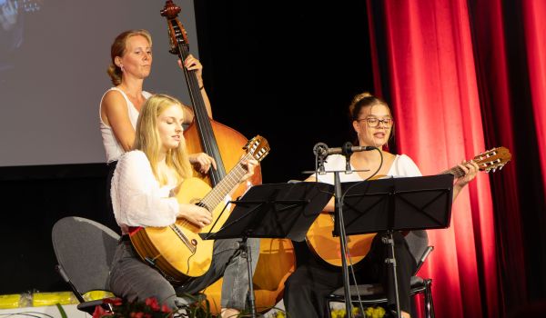 Zwei Frauen mit Gitarre und eine Frau mit Kontrabass treten auf einer Bühne auf.