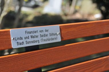 An einer Bank ist ein Metallschild angebracht. Es hat die Aufschrift: Finanziert von der Linda und Walter Seidler Stiftung Stadt Sonneberg (Treuhänderin).