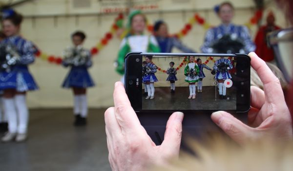 Zwei Hände filmen mit einem Smartphone Kinder, die auf einer Bühne auftreten.