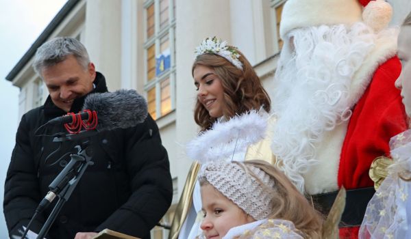 Der Bürgermeister Dr. Heiko Voigt, das Christkind und der Weihnachtsmann stehen vor einem Mikrofon.