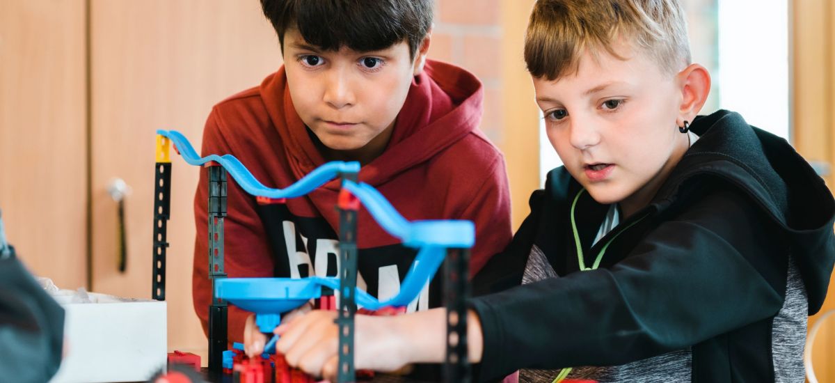 Kinder bauen eine Murmelbahn an einem Tisch.