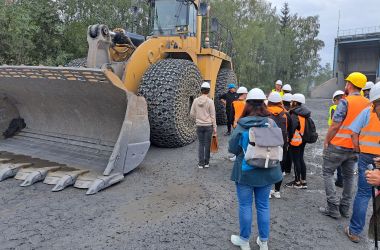 Menschen mit Helmen und Warnwesten stehen neben einem Radlader.