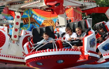 Ein rotes Karussell mit lachenden Kindern auf einem Rummel.