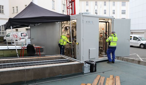 Zwei Männer in Warnjacken stehen vor einem großen Container.