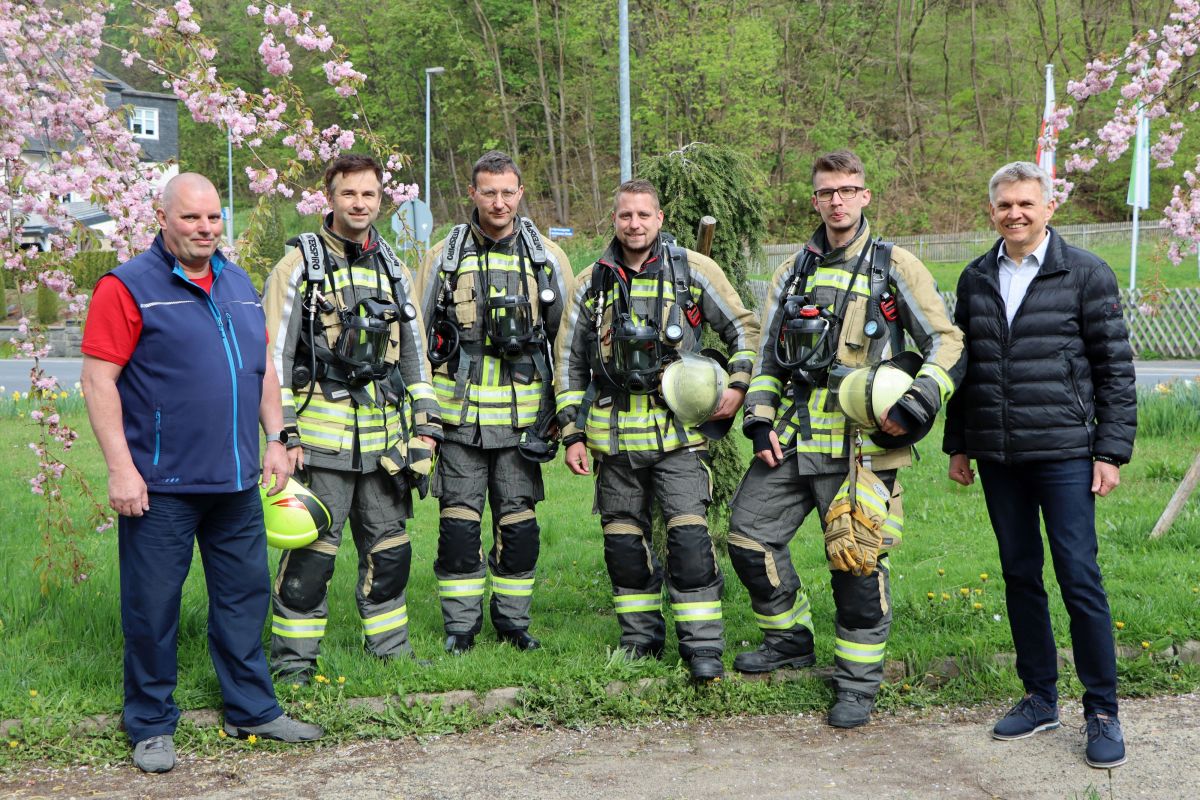 Vier Feuerwehrmänner in Schutzkleidung stehen nebeneinander. Links und rechts von ihnen steht ein weiterer Mann. Der Mann auf der rechten Seite ist der Bürgermeister Dr. Heiko Voigt.