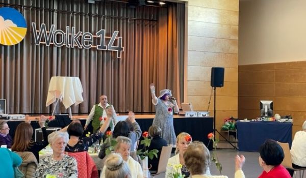 Eine Frau mit Hut steht vor einer Bühne und singt. An der Bühnenwand steht das Schild Wolke 14.