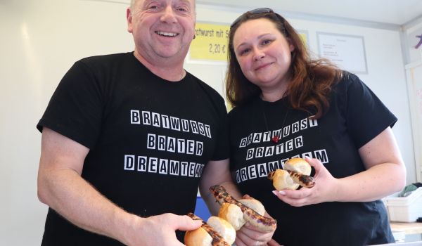 Ein Mann und eine Frau stehen in einem Verkaufsanhänger und halten Thüringerrostbratwürste in der Hand.