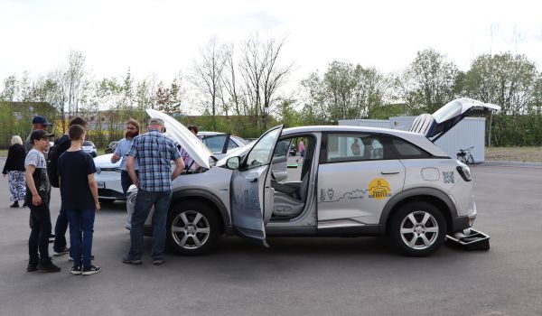 Auf einem Platz steht ein Auto. Menschen schauen sich dieses an.
