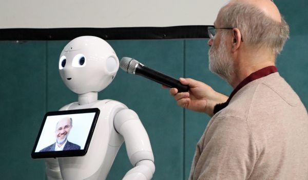 Ein Mann hält ein Mikrofon zu einem Roboter.
