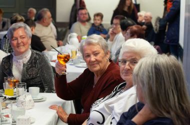 Senioren sitzen an gedeckten Kaffeetafeln in einem großen Saal.