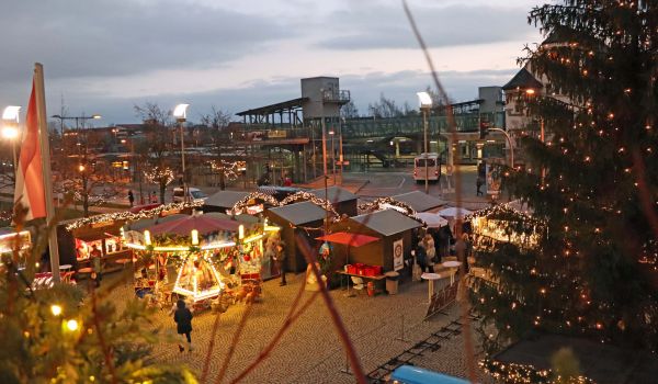 Blick vom Rathausbalkon auf einen Teil des Weihnachtsmarktes. Verkaufsstände, ein Karussell und der große Weihnachtsbaum mit Beleuchtung.