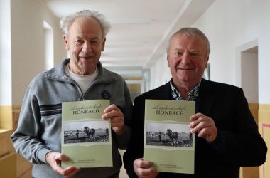Zwei Männder halten ein Buch mit der Aufschrift: Landwirtschaft Hönbach in den Händen. Darunter ist ein altes Schwarz-Weiß-Foto.
