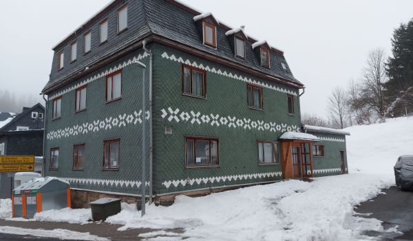 Ein dunkelgrünes Schieferhaus im Schnee.