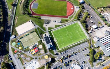 Ein Luftbild - zu sehen sind von oben ein Parkplatz, ein Fußballplatz, ein Leichtathletik-Sportfeld, Tennisplätze, eine Beachvolleyballanlage und ein Freizeitareal für Kinder und Jugendliche. Foto: J. Uebe