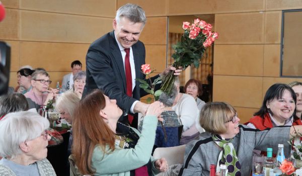 Frauen sitzen an gedeckten Kaffeetischen. Der Bürgermeister Dr. Heiko Voigt verteilt Rosen.