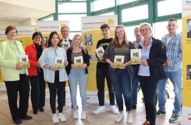 Menschen stehen nebeneinander und halten ein Buch in der Hand.