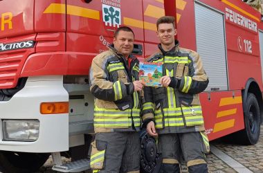 Zwei Feuerwehrkameraden stehen vor einem Feuerwehrauto.