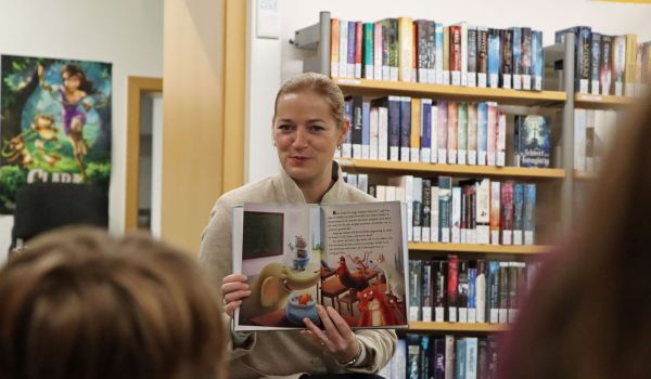 Eine Frau zeigt ein Kinderbuch mit Tieren darin. Vor ihr sitzen Kinder.
