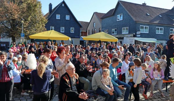 Viele Menschen sitzen draußen auf Bänken. Es scheint die Sonne.