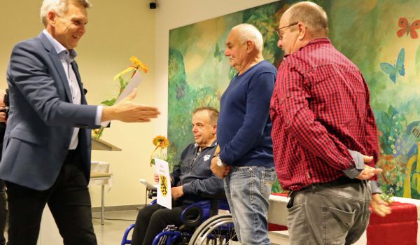 Der Bürgermeister Dr. Heiko Voigt überreicht eine Urkunde und Blumen an drei Männer.