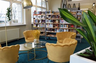 Vier gelbe Sessel stehen um einen Glastisch herum, im Hintergrund stehen Bücherregale der Stadtbibliothek Sonneberg. Gezeigt wird der seit 2024 erneuerte Aufenthaltsbereich.