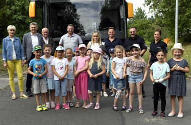 Kinder und Erwachsene stehen vor einem Schulbus auf der Straße.