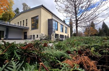 im Zentrum des Fotos steht ein gelbes Gebäude mit großen Fenstern. Es ist die Trauerhalle mit Krematorium auf dem Hauptfriedhof Sonneberg.