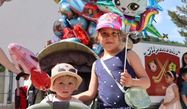 Zwei Kinder halten einen bunten Helium Luftballon in den Händen.