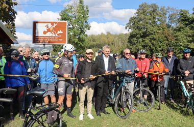 Eine große Traube Radsportler steht hinter einem gelb-schwarzen Band, das von vier Männern mit Scheren durchtrennt wird.
