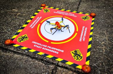 Eine rote Plane mit der Aufschrift: Freiwillige Feuerwehr Stadt Sonneberg. In der Mitte befindet sich das Logo des Sonneberger Reiterleins. Darauf steht eine Drohne.