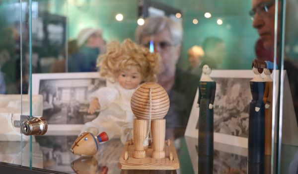 Holzspielzeuge und eine Puppe in einer Vitrine.