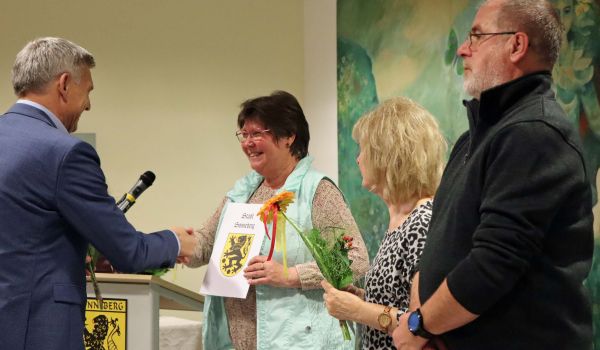 Der Bürgermeister Dr. Heiko Voigt überreicht eine Urkunde und Blumen an zwei Frauen.
