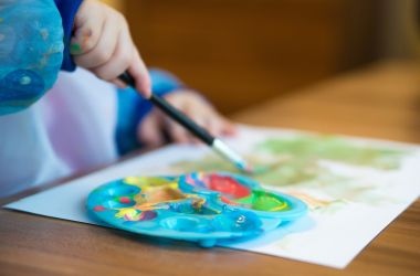 Ein Kind malt mit einem Pinsel auf ein Blatt Papier.