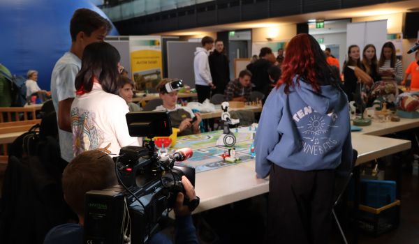 Auf einem Tisch stehen kleine Roboter. Außenrum stehen Jugendliche.