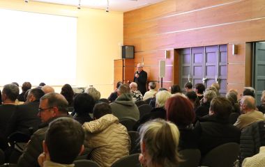 Viele Menschen sitzen in Stuhlreihen in einem Saal.