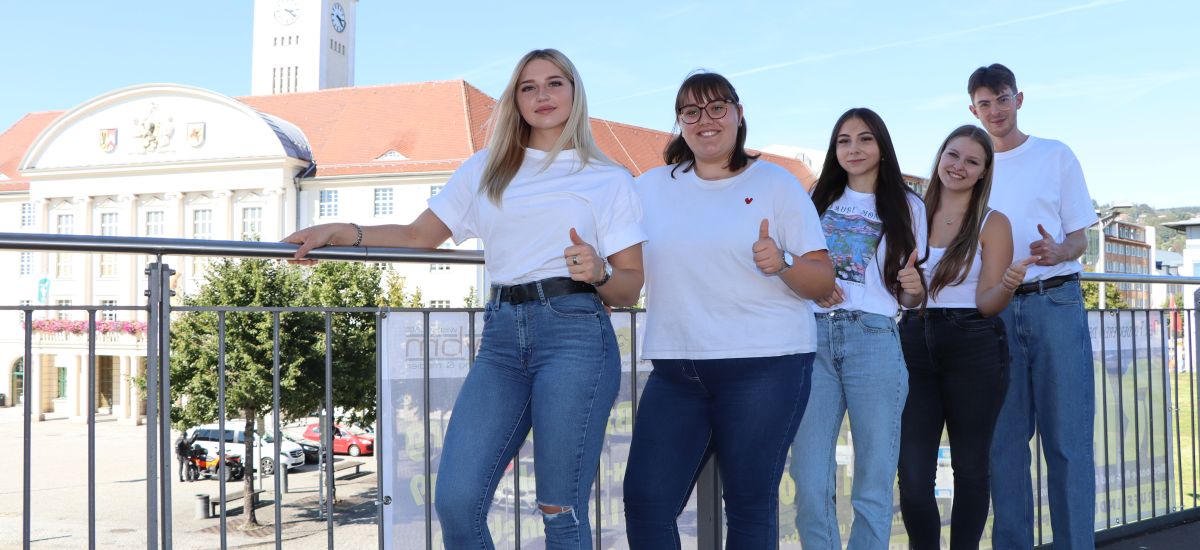 Fünf junge Menschen stehen an einem Geländer. Es sind Auszubildende der Stadtverwaltung. Im Hintergrund ist das Rathaus der Stadt Sonneberg zu sehen.