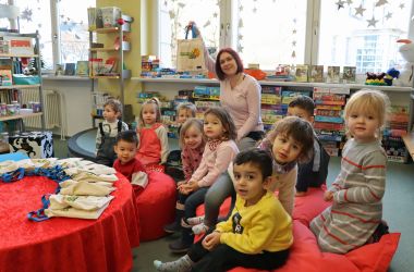 Kleine Kinder und eine Frau sitzen auf Sitzkissen in der Bibliothek.