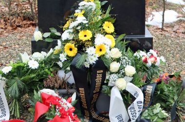 Ein Grabstein mit Trauerschmuck davor.