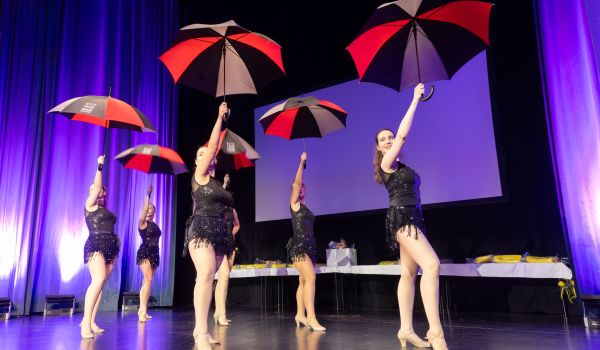 Frauen tanzen mit Regenschirmen auf einer Bühne.