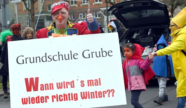 Ein Clown hält ein Schild mit der Aufschrift: Grundschule Grube, Wann wirds mal wieder richtig Winter?