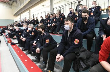 Eine Gruppe von Menschen in Feuerwehruniform sitzt auf einer Tribüne.