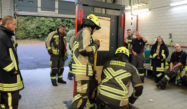 Mehrere Feuerwehrkameraden schauen zu, wie eine Übungstür geöffnet wird.